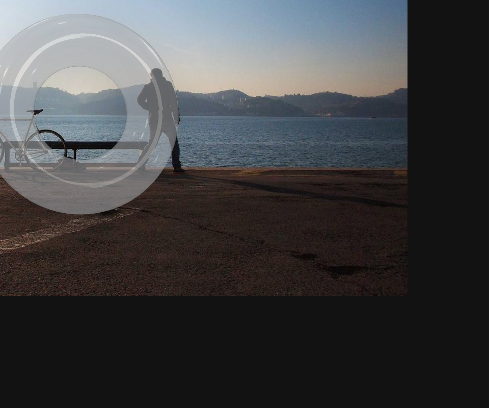 A clear glass torus standing over a seaside photograph, its thickness and highlights visible, the scene showing through it